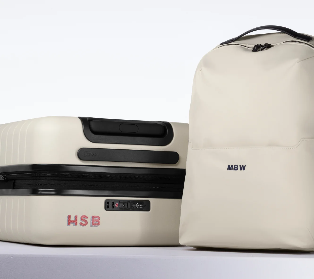 Two beige suitcases with visible monogrammed initials on a white background