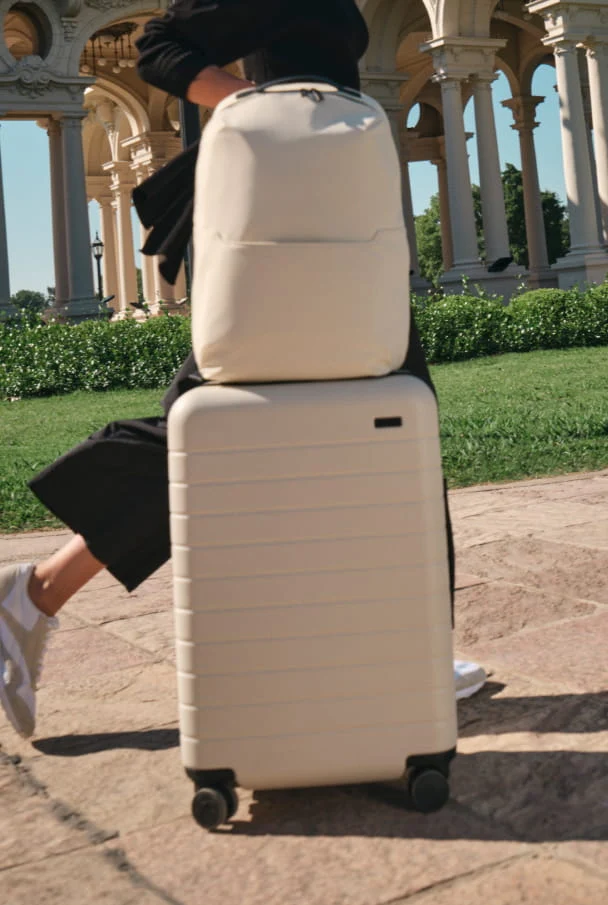 Person with a white suitcase and backpack in an outdoor setting