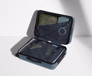 The Bigger Carry-On suitcase in Coast Blue shown open on its side and packed with Away's packing organizers to show capacity and the interior compression system, designed to help you pack more in