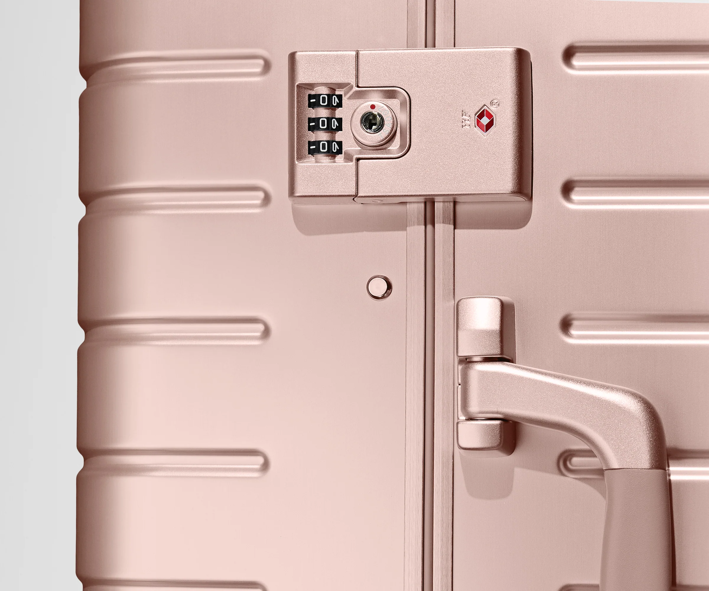 Close up view of the TSA lock on the side of a Rose Gold Aluminum suitcase
