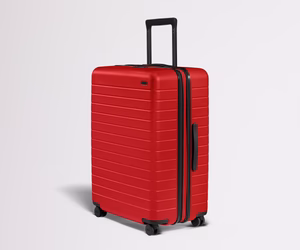 Red suitcase with black handle and wheels on a light gray background