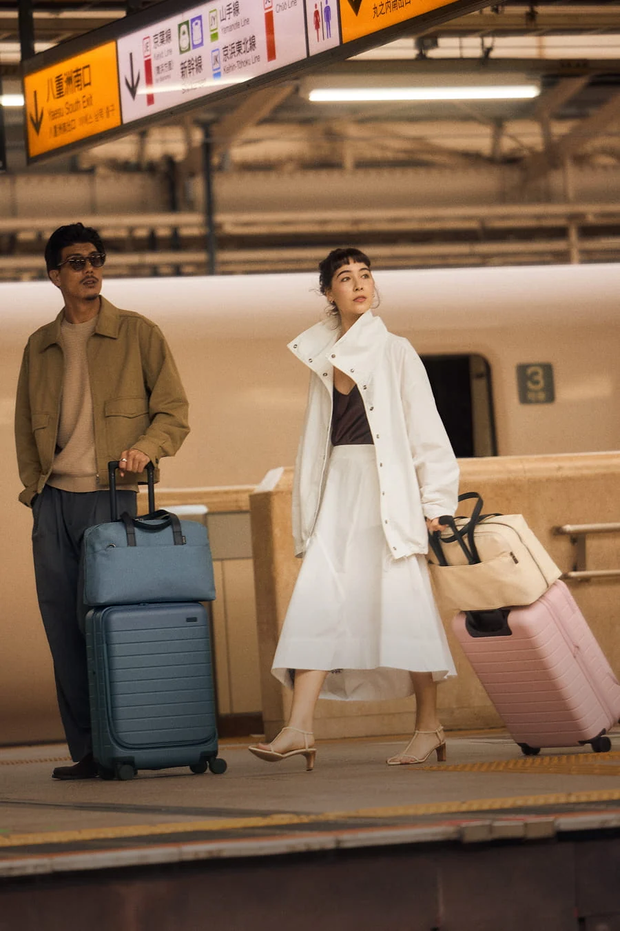 Two people with luggage at a train station platform.